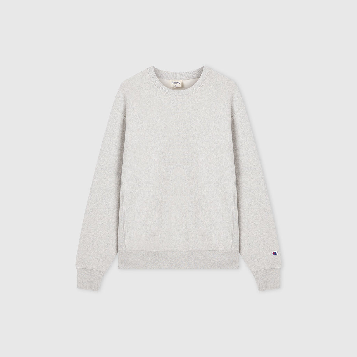 The Men’s Relaxed Fit Crewneck Sweatshirt by Champion is a plain light grey long-sleeve crewneck featuring ribbed cuffs and waistband, displayed on a white background. Made from heavyweight fleece in the signature Reverse Weave style, it includes a small Champion logo on the left sleeve near the cuff.