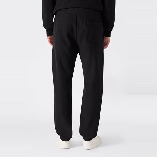 A person is shown from the back against a plain light background, wearing black Champion Men’s Knitted Elastic Cuff Pants—designed in a classic sportswear fleece style with an elastic waistband and single back pocket—and white shoes.