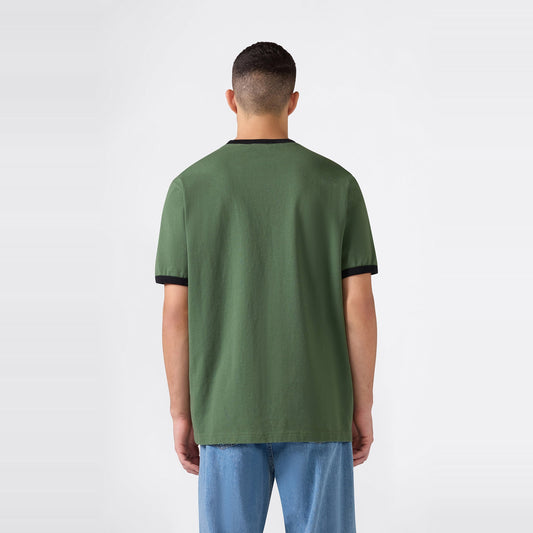 A man with short dark hair wearing a Champion Men’s Knitted Ringer T-Shirt in green with black trim and light blue jeans stands facing away against a plain white background.