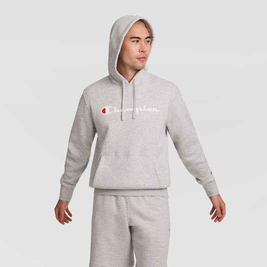 A person wearing a light gray Champion Powerblend Hoodie with the Full Script Logo and matching sweatpants stands with arms slightly out, looking to the side against a plain light background.