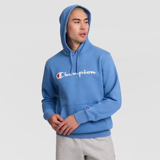 A person wearing a blue Champion Powerblend Hoodie, Full Script Logo, with the hood up and gray sweatpants looks to the side against a plain light background.