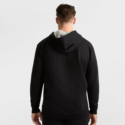 A man faces away from the camera, wearing a Champion Powerblend Hoodie, C Logo - Big & Tall in black with the hood down, set against a plain white background.
