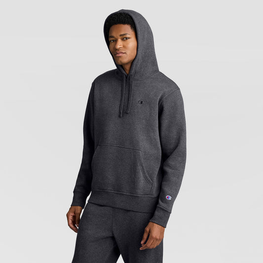 A person wearing a dark gray Champion Powerblend Hoodie, C Logo, along with matching sweatpants stands against a plain light gray background, looking slightly to the side with a neutral expression.