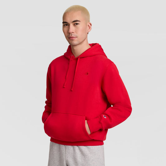 A person wearing a bright red Champion Powerblend Hoodie, C Logo, featuring a front kangaroo pocket and a small logo on the chest and sleeve.