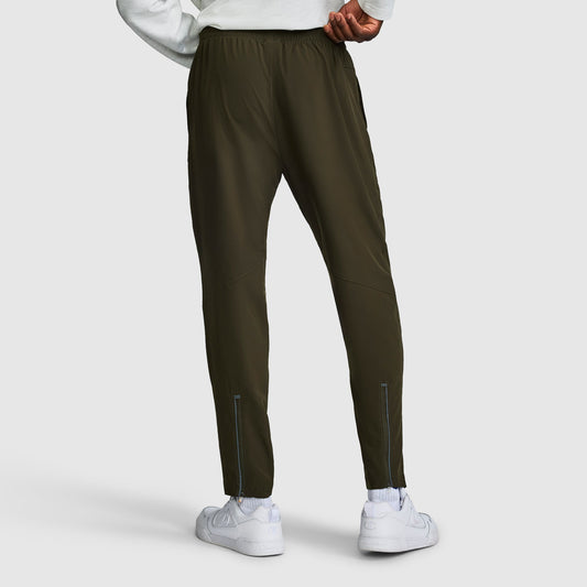 A person is shown from the back wearing dark green Champion MVP Pants, Moisture Wicking, C Logo men’s slim-fit sweatpants, paired with a white sweatshirt and white sneakers. The pants feature reflective details near the ankles and are crafted from moisture-wicking fabric for comfort during any activity.