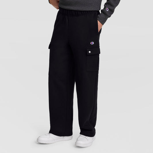 A person wearing Champion Fleece Cargo Pant, C Logo in black streetwear style pairs them with white sneakers, hands in pockets. The pants feature side cargo pockets and a small Champion “C” logo near the waist. Only the lower half is visible, drawing attention to the comfortable cotton-polyester fleece design of these Champion cargo pants.