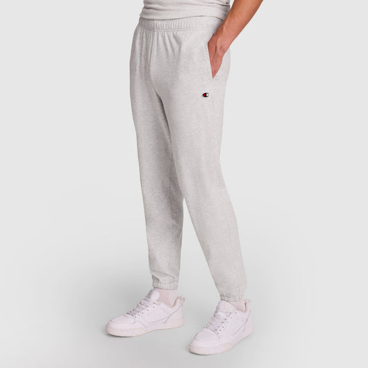 A person wears Champion Lightweight Lounge Pants with a cinched hem and C logo on the left thigh, styled with white sneakers and a hand in their pocket, standing against a plain white background.