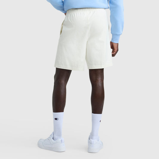 A person is seen from the back against a white background wearing Champion 9" Lightweight Lounge Shorts with a C Patch Logo, a light blue sweatshirt, white crew socks featuring a blue Champion logo, and white sneakers.