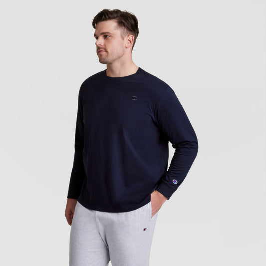 A man in a navy Champion Classic Long Sleeve T-Shirt, Embroidered C Logo - Big & Tall, and light gray sweatpants stands against a plain background, looking left with hands in pockets for a sporty, relaxed vibe.