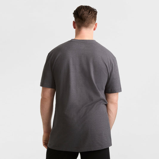 A man faces away from the camera, wearing a Champion Classic T-Shirt, C Logo - Big & Tall in dark gray with black pants, set against a plain white background.