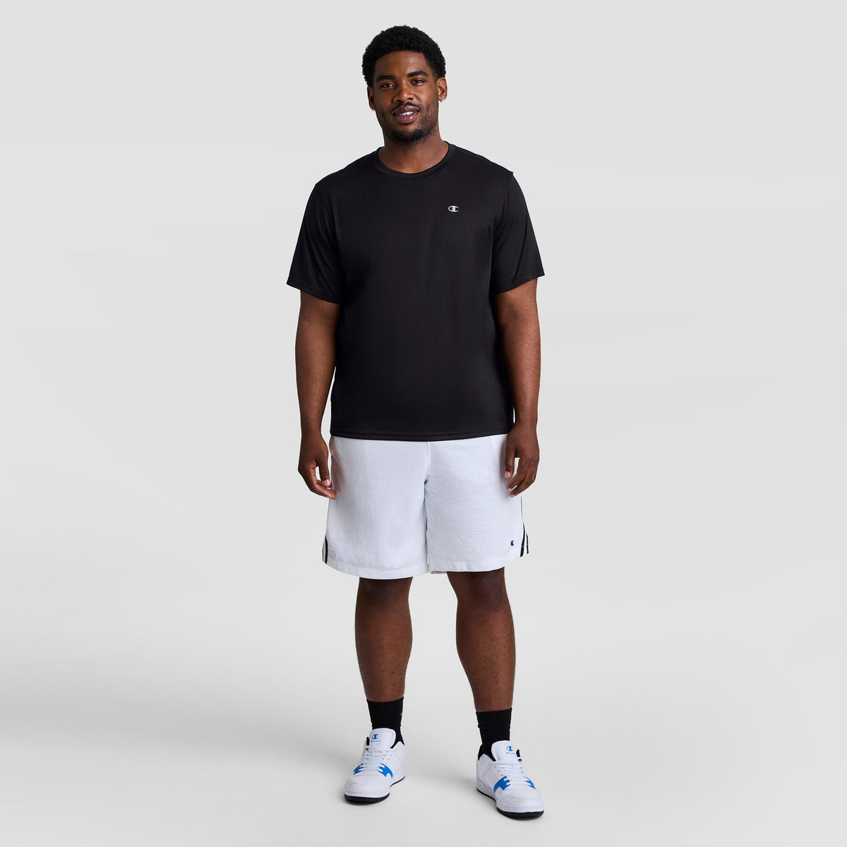 A man wearing a black Sport T-Shirt, Reflective C Logo - Big & Tall with a small logo on the chest, white athletic shorts, and white sneakers.