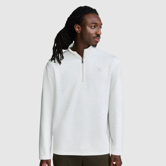 A man with long dreadlocks is wearing a light gray Champion Sport Long Sleeve 1/4 Zip Mockneck featuring the C logo. He stands against a plain light gray background, looking to his left with a neutral expression.
