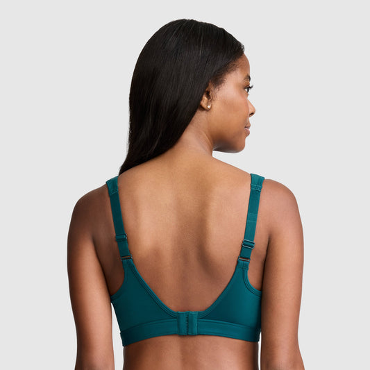 A woman with long dark hair, shown from the back against a plain light gray background, models the Champion Spot Comfort High-Impact Sports Bra, C Logo in teal, featuring adjustable straps and a hook-and-eye closure.