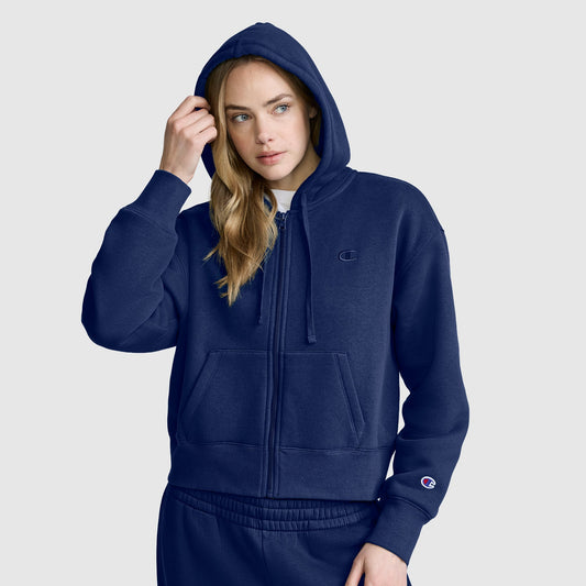 A person wearing a Champion Cropped Zip-Up Hoodie in navy blue with the hood up and matching sweatpants stands against a plain light gray background.