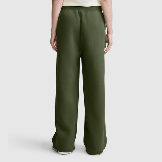 A person is shown from the back, standing against a plain light gray background, wearing the Champion Wide Leg Fleece Sweatpants with C Logo in dark green and a white shirt.
