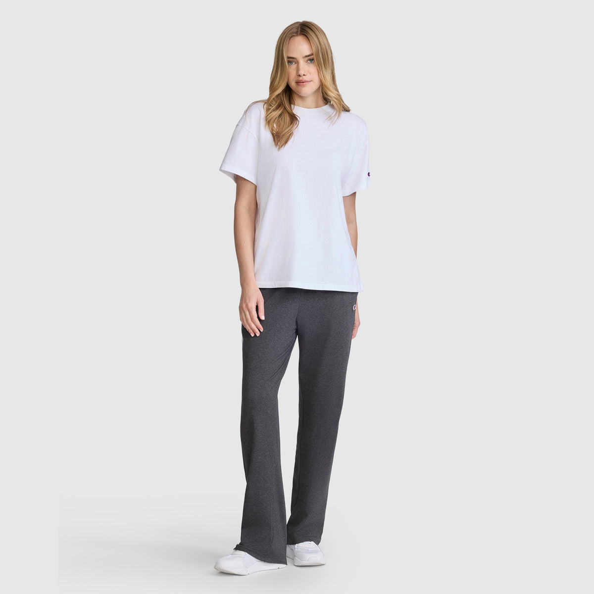 A woman wearing a white t-shirt and charcoal grey Champion Lightweight Lounge Pants, C Logo with a small logo on the hip.