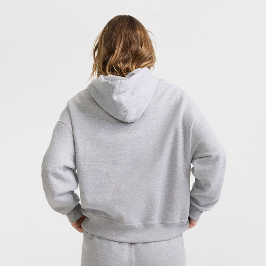 A person with light brown hair is seen from behind, wearing a gray Champion Powerblend Crewneck Sweatshirt with a script logo, standing against a plain white background.