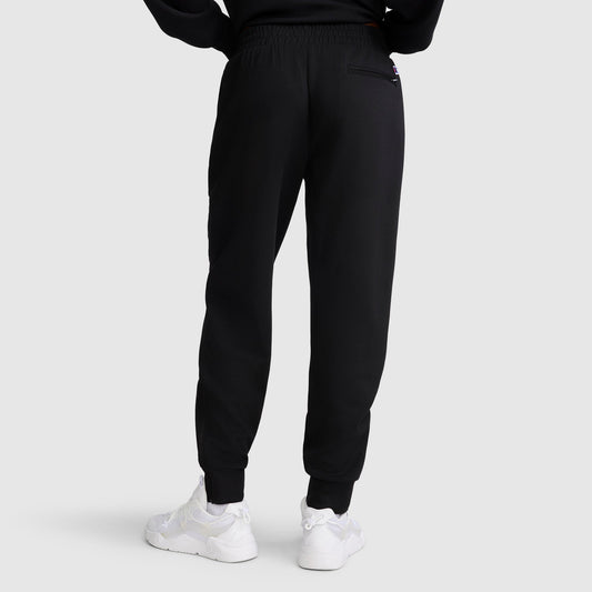 A person is seen from the back, standing against a plain light gray background, wearing the Champion Taper Leg Jogger with Zippers in black paired with white sneakers.