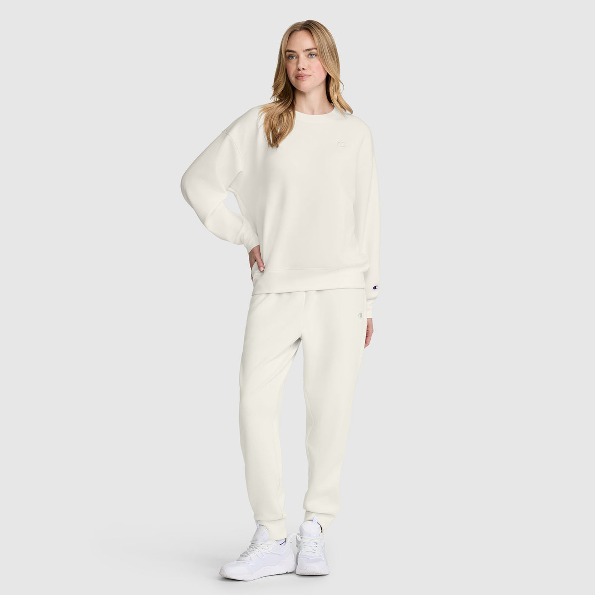 A person wearing a matching off-white Champion Crewneck Pullover Sweatshirt and sweatpants with white sneakers.