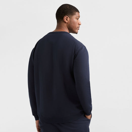 A man faces away from the camera, wearing a dark navy Champion Powerblend Crewneck Sweatshirt, C Logo - Big & Tall and matching pants, set against a plain white background.