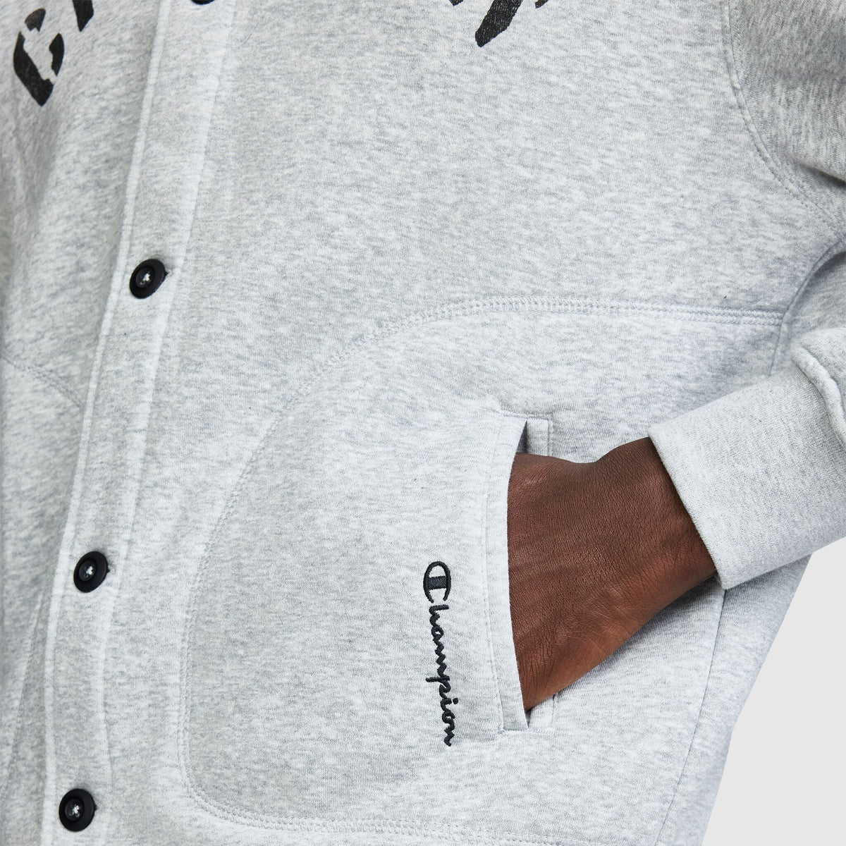 Close-up of a person with their hand in the pocket of a grey Champion Fleece Baseball Jacket.