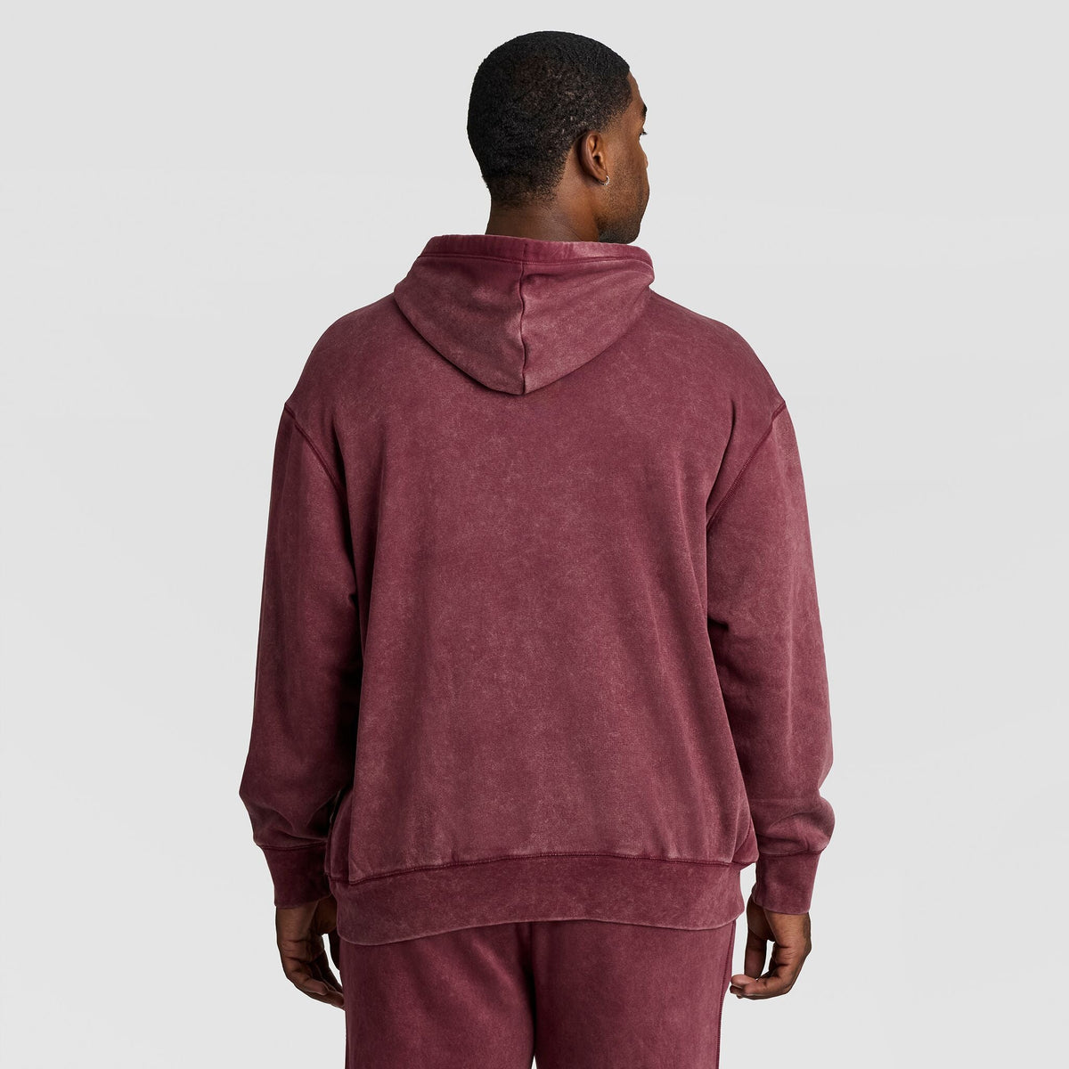 A man viewed from behind, wearing a maroon Mineral Wash Pullover Hoodie, C Patch Logo.