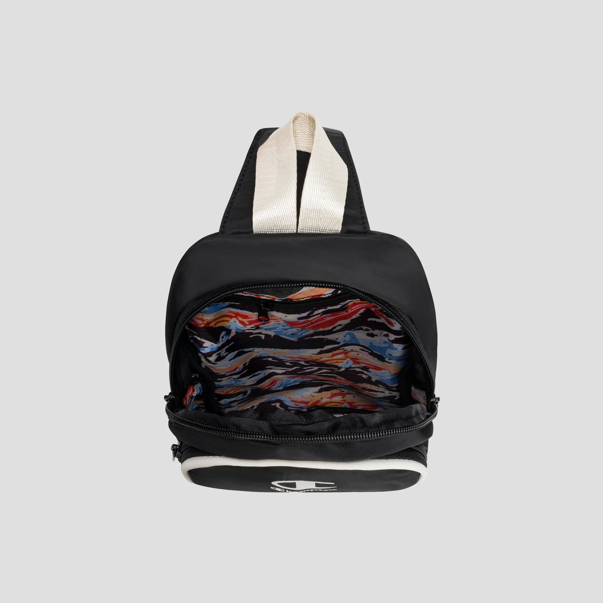 The Champion Oracle Sling Pack, a compact black bag with beige straps, is open to display its vibrant, abstract-patterned interior lining. Reminiscent of a small gym bag, this accessory stands out against the plain gray background.