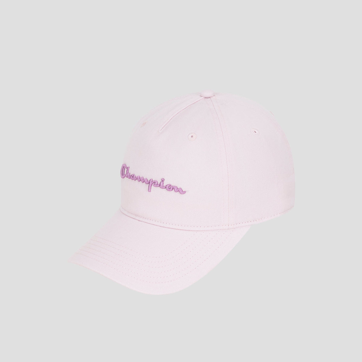The Script Embroidery Adjustable Cap by Champion is crafted from premium cotton twill in a light pink hue, featuring the word “Champion” embroidered in purple cursive on the front. The cap is displayed against a plain light gray background.