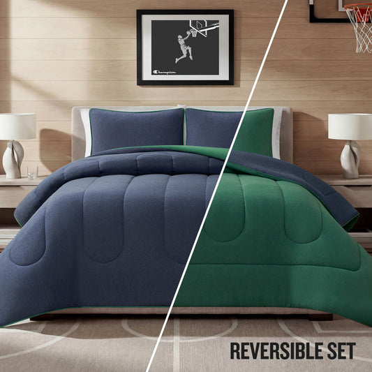 A neatly made bed features the Champion Premium Reversible Solid Jersey Comforter Set in blue and green, matching pillows, two bedside tables with lamps, and a framed basketball artwork above the headboard. The text “REVERSIBLE SET” appears at the bottom right.