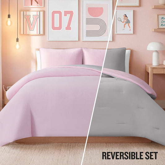A bedroom styled with Champion’s Reversible Solid Jersey Comforter Set—cozy bedding that features pink on one side and gray on the other. Modern wall art, ambient lighting, and a compact desk complete the look. Text reads REVERSIBLE SET.