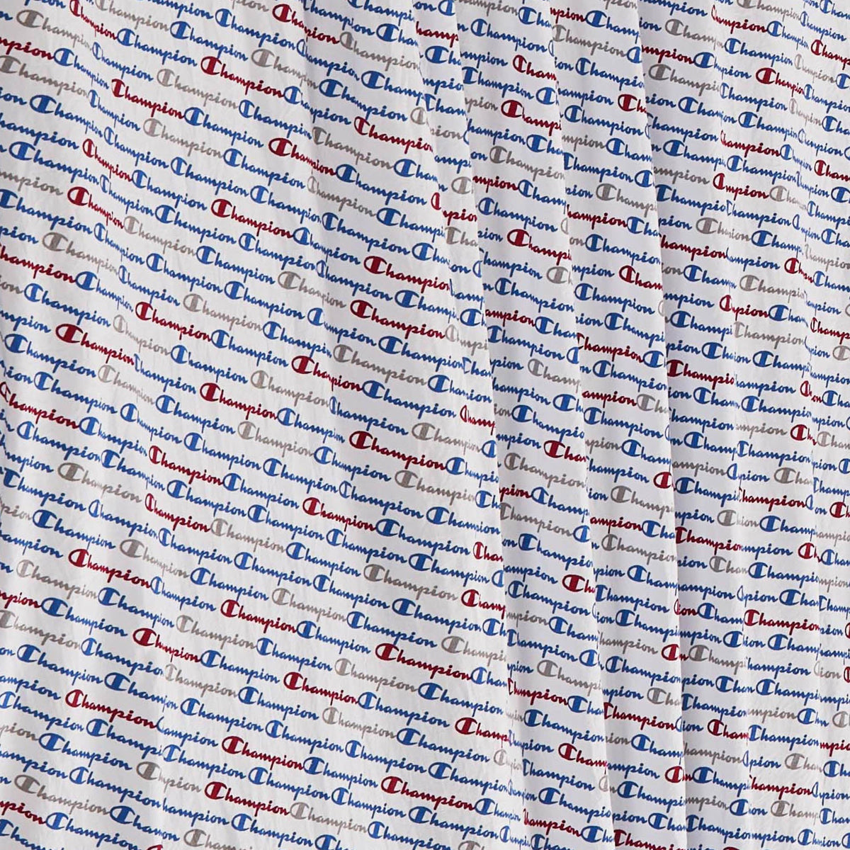 Close-up of the super-soft Printed Microfiber Sheet Set by Champion, featuring a repeating blue and red Champion logo pattern on a white background. Light wrinkles and folds in the fabric enhance the cozy appeal of these branded sheets.