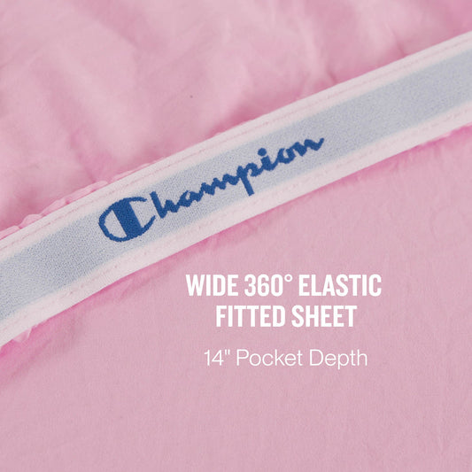 A close-up of a pink Champion Peak Comfort Microfiber fitted sheet with a wide 360° elastic band showcases the athletic bedding, featuring text stating WIDE 360° ELASTIC FITTED SHEET 14” Pocket Depth. Part of the Champion Peak Comfort Microfiber Sheet Set, these deep pocket sheets ensure a secure and comfortable fit for your mattress.