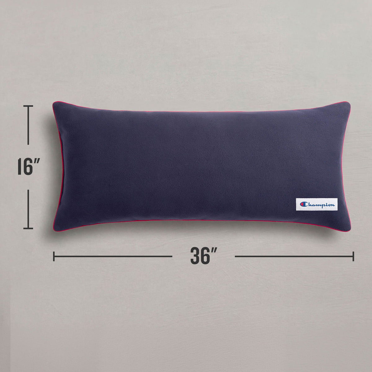A Champion Faux Wool Body Pillow in a rectangular navy blue design with red piping, measuring 16 by 36 inches, rests on a gray surface. This cozy accent from Champion features a small branded logo tag on the corner, making it an ideal addition to any space.