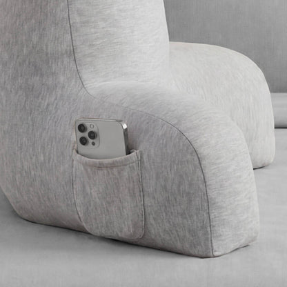 A close-up of the Champion Jersey Backrest Pillow in gray, featuring a small pocket on the armrest that holds a silver smartphone. The gray background blends seamlessly with the pillow, creating a comfortable and signature Champion look.