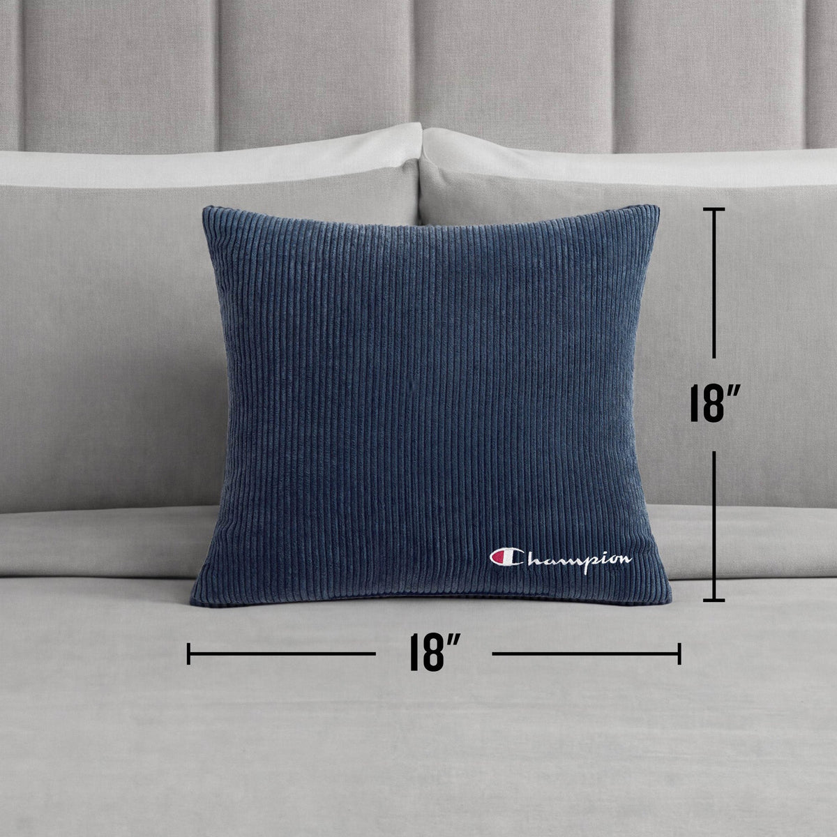 A Champion 18" x 18" Logo Pillow in blue corduroy rests on a light gray bed with a headboard in the background, bringing a casual Champion style to the room.