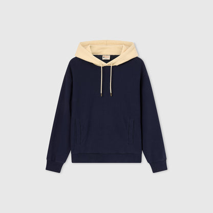 A Champion Women’s Knitted Hooded Sweatshirt in navy blue with a beige hood and beige drawstrings, displayed on a plain light gray background. This sweatshirt features heavyweight fleece for added warmth, along with a front pocket and ribbed cuffs.