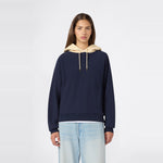 A person wearing the Champion Women’s Knitted Hooded Sweatshirt in navy blue, featuring a beige hood and heavyweight fleece construction, paired with light blue jeans, stands facing forward against a plain white background.