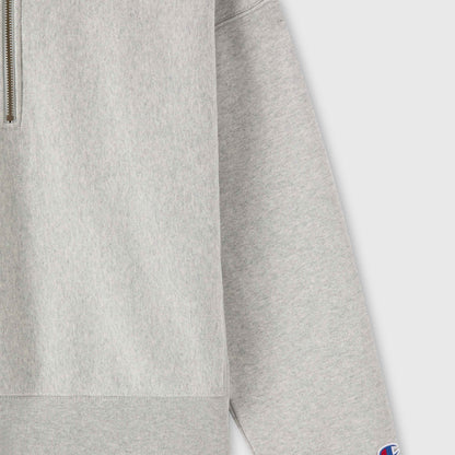 Close-up of a light gray Champion Women’s Knitted Half Zip Sweatshirt with long sleeves. A small patch featuring the blue and red Champion logo is visible on the cuff, highlighting this essential piece of women’s sportswear.