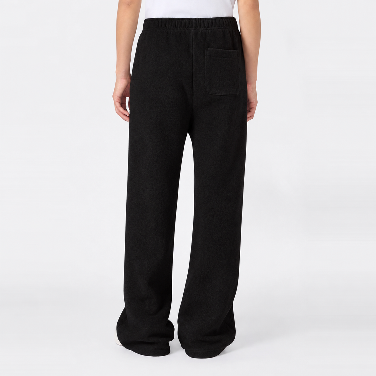 A person is seen from the waist down, standing against a plain white background, wearing Champion Women’s Knitted Flare Pants—loose-fitting black trousers featuring an elastic waistband and back pocket for a modern twist on classic sportswear style.