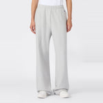 A person wearing Champion Women’s Knitted Flare Pants in a loose-fit, light gray style, paired with a white t-shirt and white sneakers, stands against a plain white background. The heavyweight fleece fabric of these flared pants adds an elevated touch to this classic women’s sportswear look.
