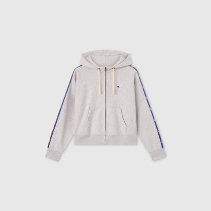 The Women’s Icon Hooded Full Zip Sweatshirt by Champion is a light gray heavyweight fleece zip-up hoodie with a hood and drawstrings, featuring small logos along blue stripes down each sleeve. This hoodie has front pockets and ribbed cuffs and hem, displayed on a plain white background.
