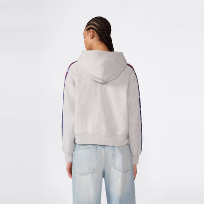 A person with braided hair is standing with their back to the camera against a plain background, wearing light blue jeans and a light gray Champion Women’s Icon Hooded Full Zip Sweatshirt featuring patterned stripes on the sleeves.
