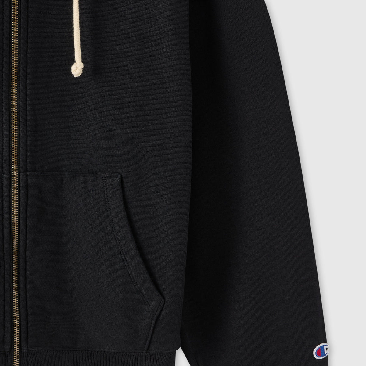 Close-up of a Women’s Icon Hooded Full Zip Sweatshirt by Champion in black heavyweight fleece, with a pocket, beige drawstring, ribbed hem, and small embroidered Champion logo on the sleeve.