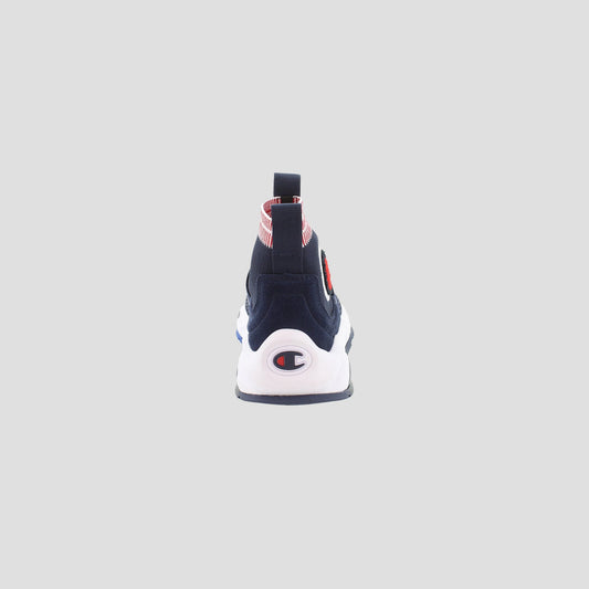 The Champion Kids' Rally Pro slip-on shoe is shown from the back, highlighting its navy upper, white sole, Champion logo on the heel, and a red and white striped pull tab. The background is plain light gray.