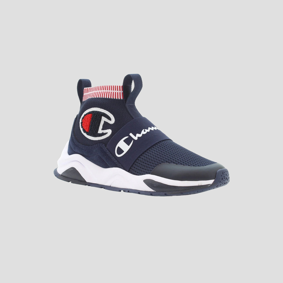 The Kids' Rally Pro by Champion is a navy slip-on shoe with a white sole, red and white striped ankle, and prominent Champion logo on the side and strap, shown against a light gray background.