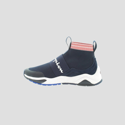 The Champion Kids' Rally Pro is a navy blue knit sneaker with a white sole, black accents, a wide strap with “Champion” in white, and a red-and-white striped ankle collar, shown on a light gray background.