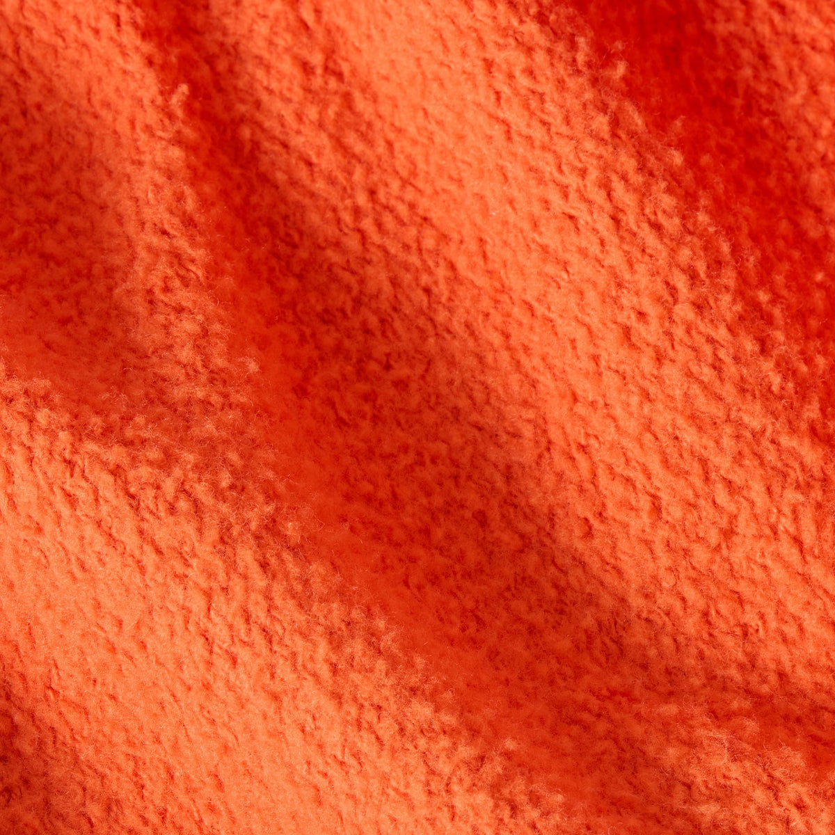 A close-up of textured orange fabric with soft shadows and visible fuzzy fibers, highlighting the Reverse Weave fleece featured in the Men’s Knitted Polo Neck Sweatshirt by Champion, and showcasing the material’s warmth and intricate detail.