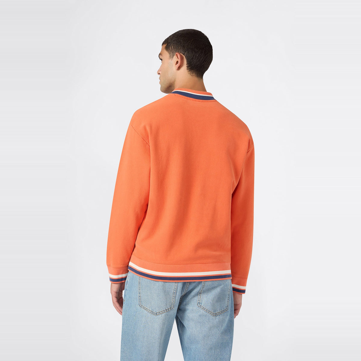 A man is seen from behind, wearing the Champion Men’s Knitted Polo Neck Sweatshirt in orange featuring white and blue trim, paired with light blue jeans against a plain white background.