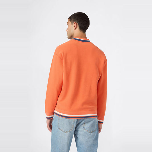 A man is seen from behind, wearing the Champion Men’s Knitted Polo Neck Sweatshirt in orange featuring white and blue trim, paired with light blue jeans against a plain white background.