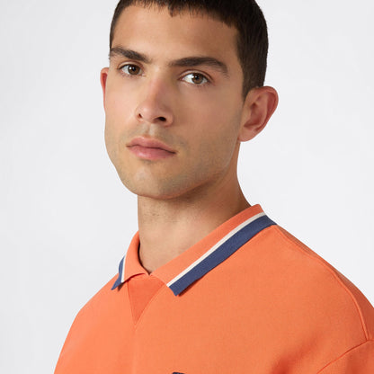 A young man with short dark hair models the Champion Men’s Knitted Polo Neck Sweatshirt in orange with blue and white trim, showcasing contemporary men’s sportswear against a plain light background.